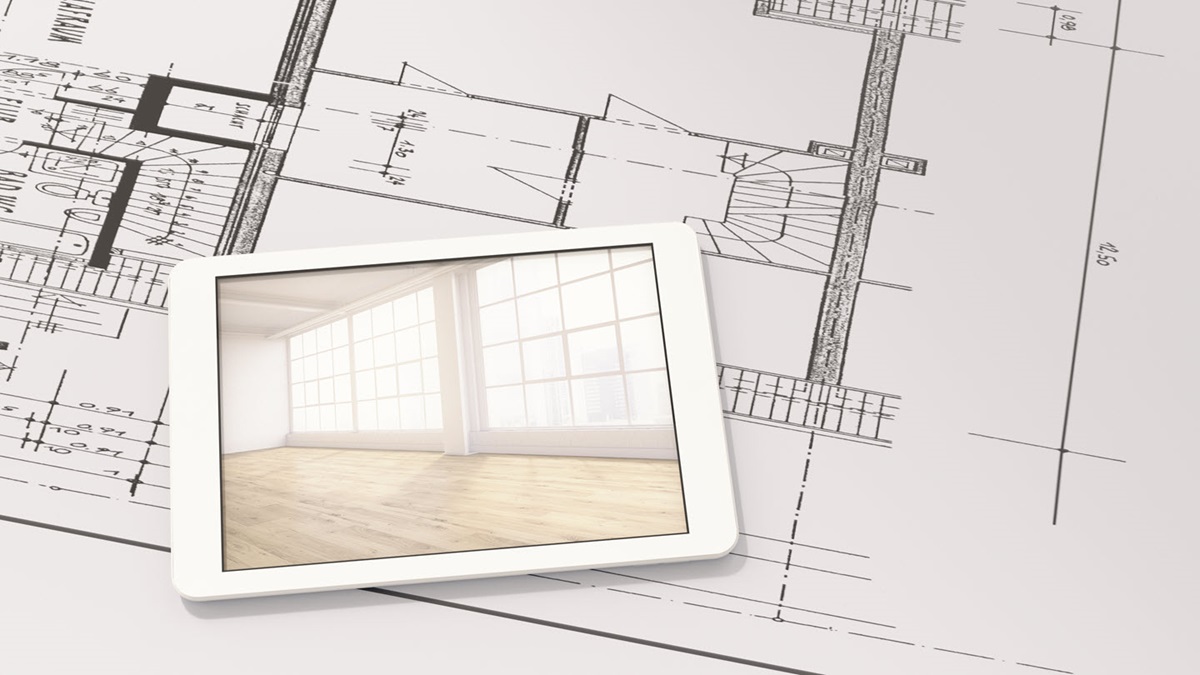 A tablet showing the interior of a completed building lays atop an architectural blueprint.