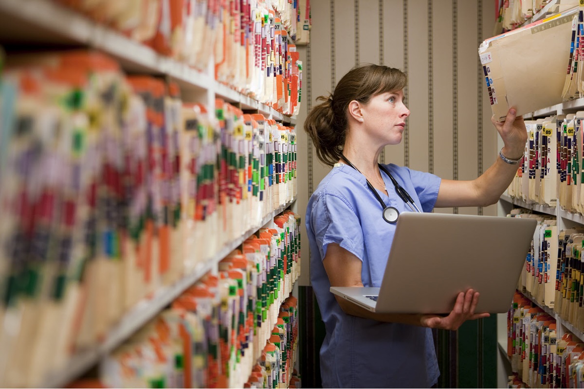 A doctor continues her hospital's digitization of medical records and grabs a file folder from a high shelf.