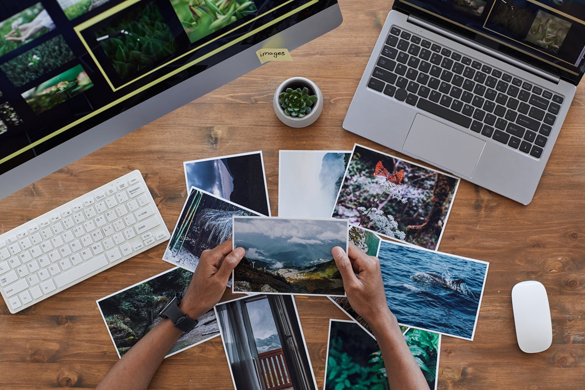 Person looking through photos and comparing them with digital versions on their computer monitor. 