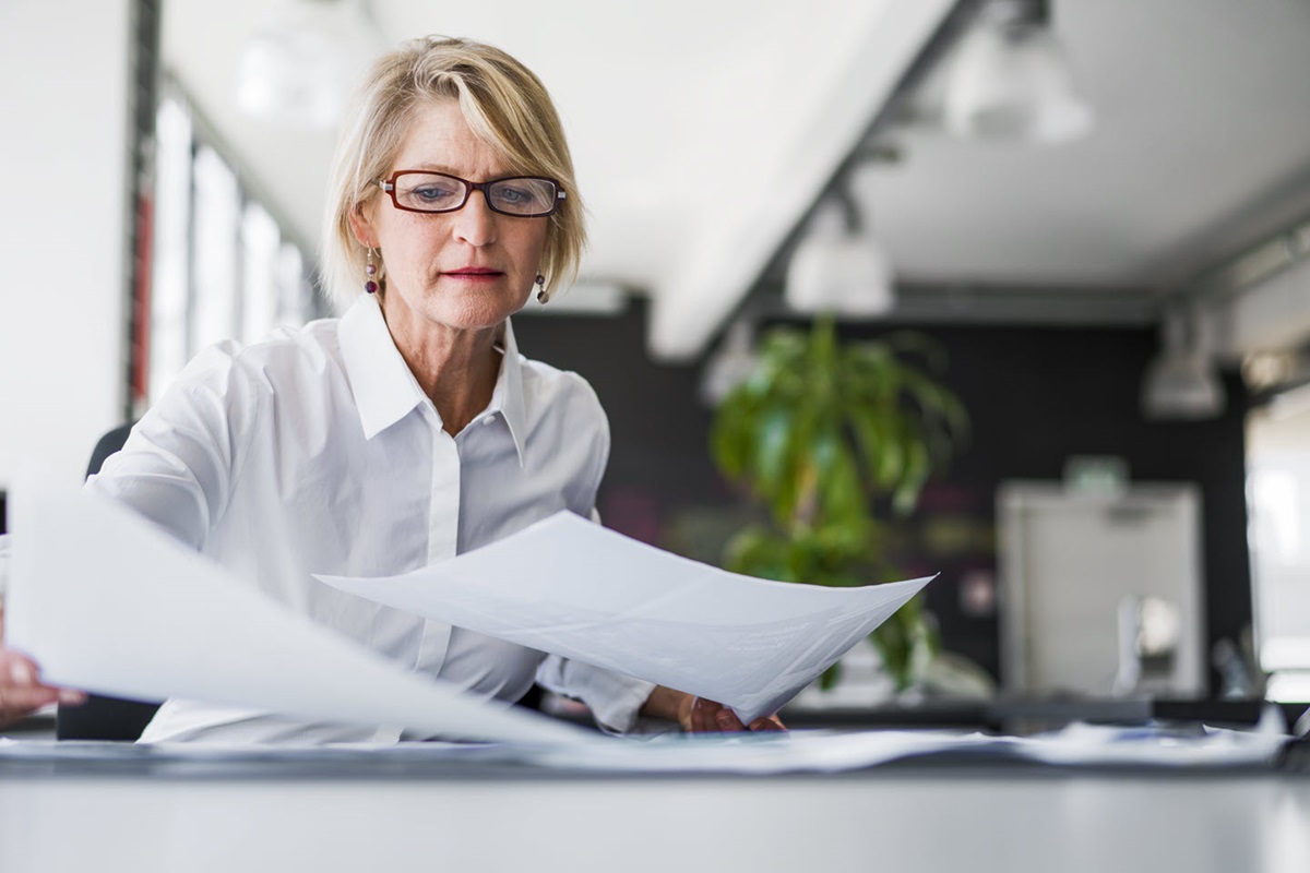 A businesswoman sorts through paper documents at her desk.