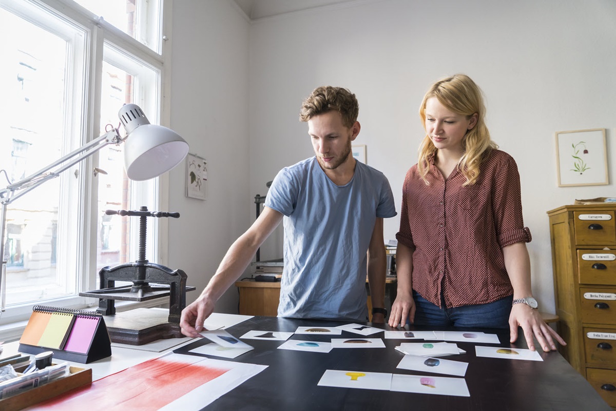 A man and woman look through product photos in a small office.