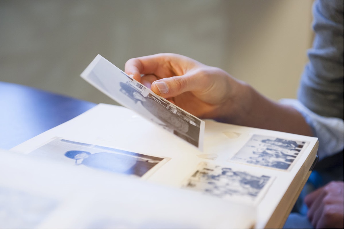 A woman's hand holds a black-and-white photo of a child in front of a photo album.