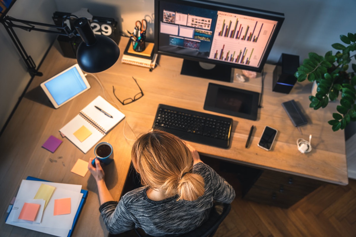 An aerial view of a home office with a woman sitting at her desk with a cup of coffee.