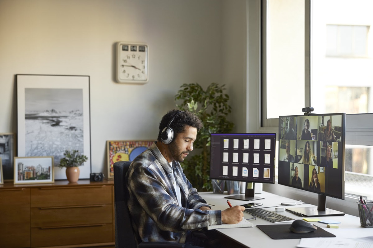 A person wearing headphones sits in a bright, well-decorated home office space and takes notes during a video conference.
