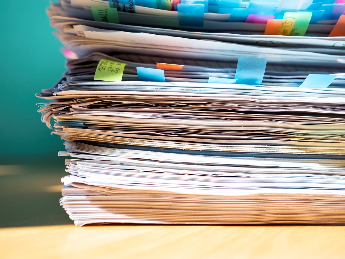 A close-up on a stack of papers, files, and folders with a myriad of sticky notes and bright bookmarks sticking out to the side.