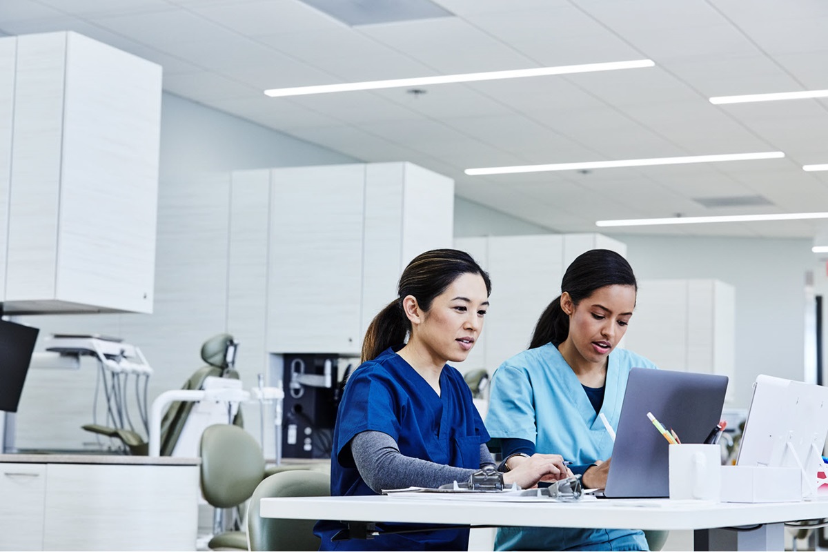 Hygienists using laptop together at desk in dental clinic.