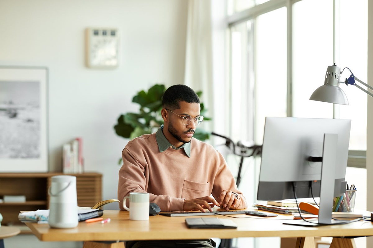 A remote worker looks at their computer screen, surrounded by a bright and welcoming home office.
