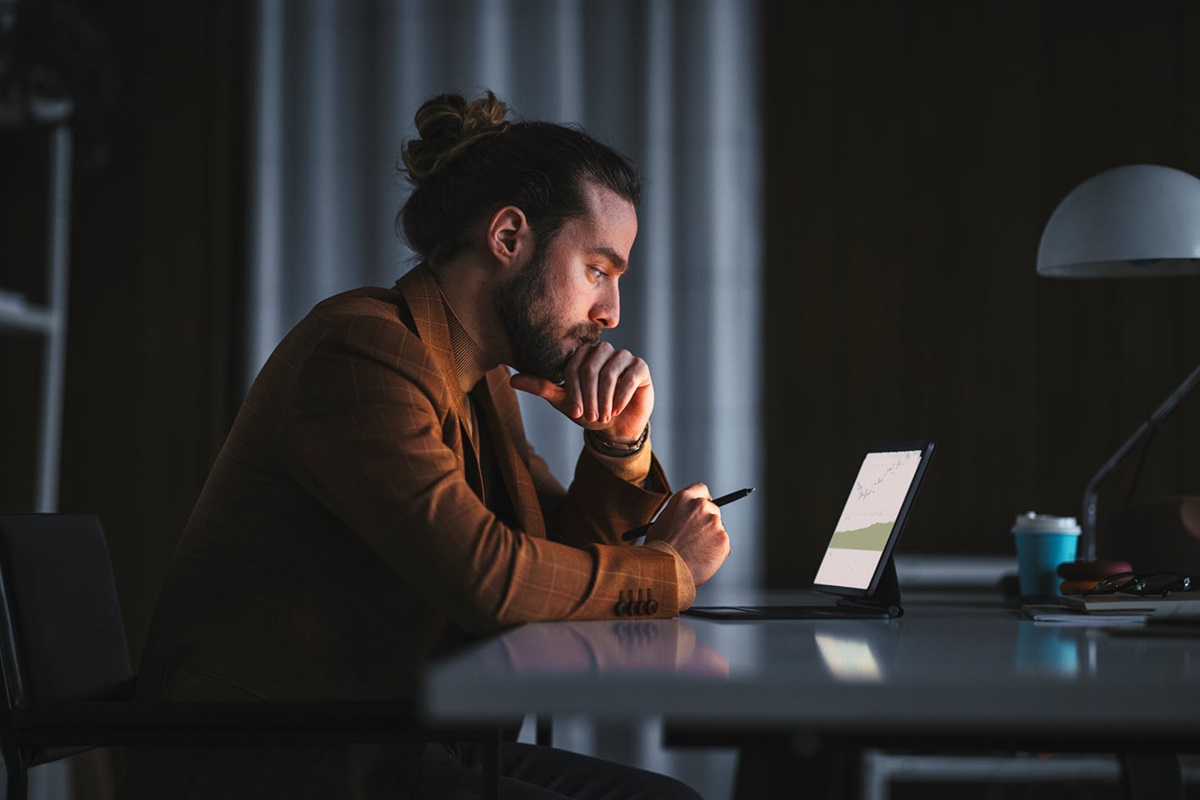 A man sits in a dark room looking at a small monitor on a table.