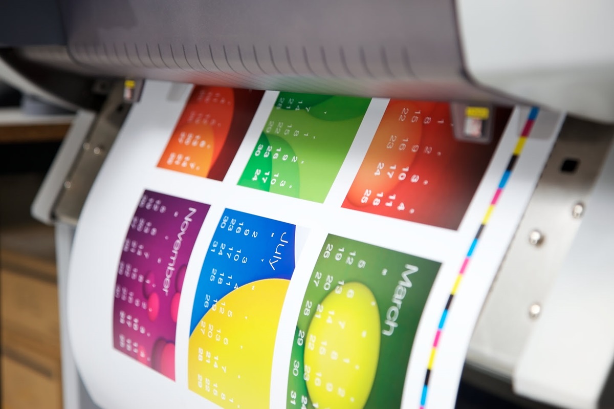 A colorful calendar hangs from the output slot of a printer.