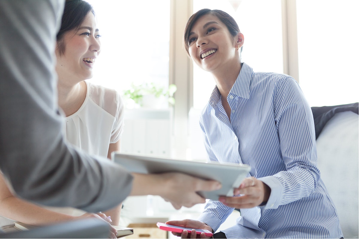 A smiling woman hands papers to a person off-camera.