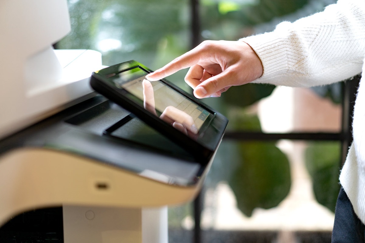 A hand uses the touchscreen control pad of an office printer.