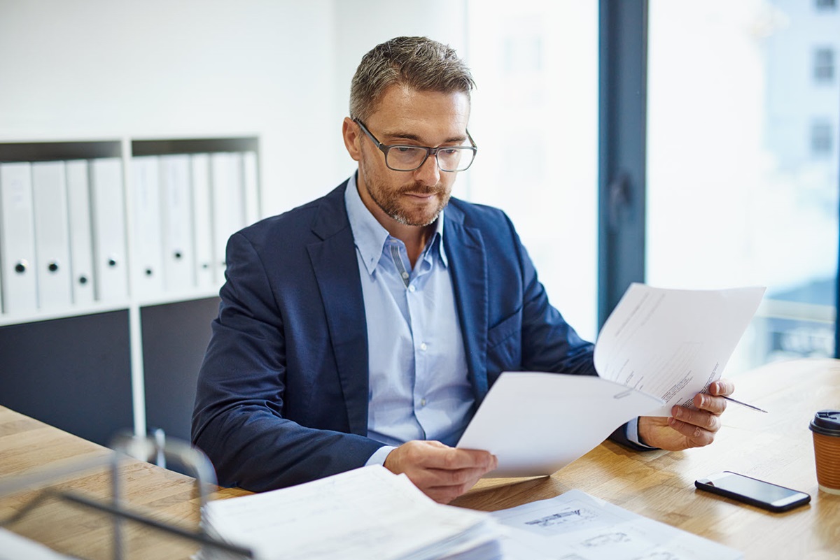 A well-dressed businessman sorts through work documents in a brightly lit office.