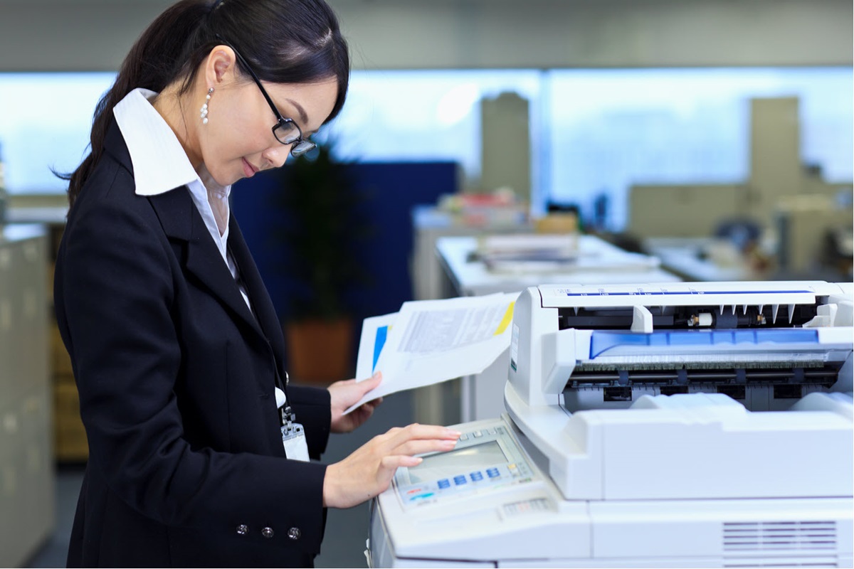 A woman in an office inputs commands on a standing printer's touchscreen.