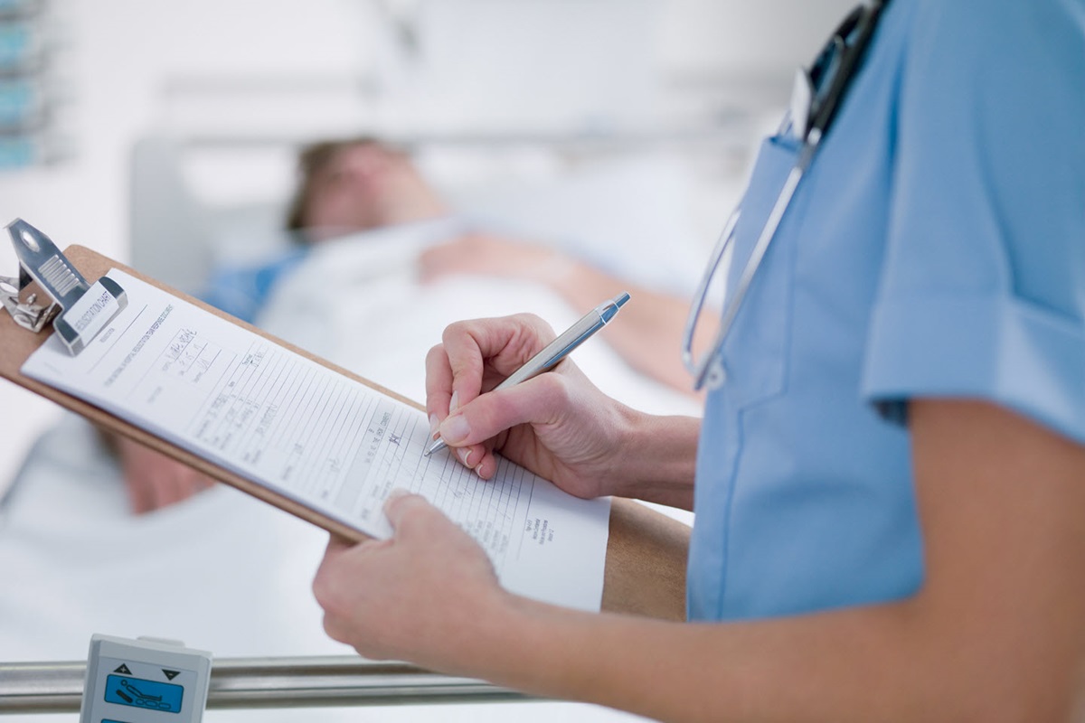 A nurse fills out a patient intake form attached to a clipboard.