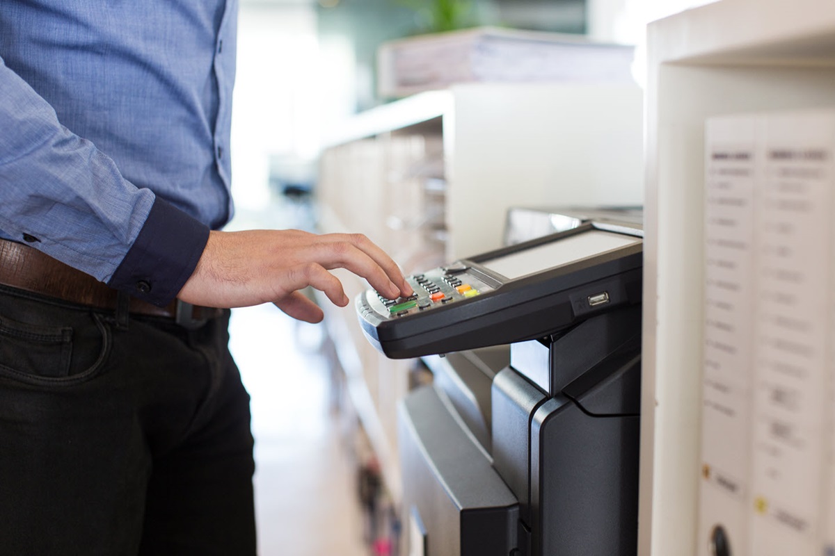 A man operates a printer in an office setting.