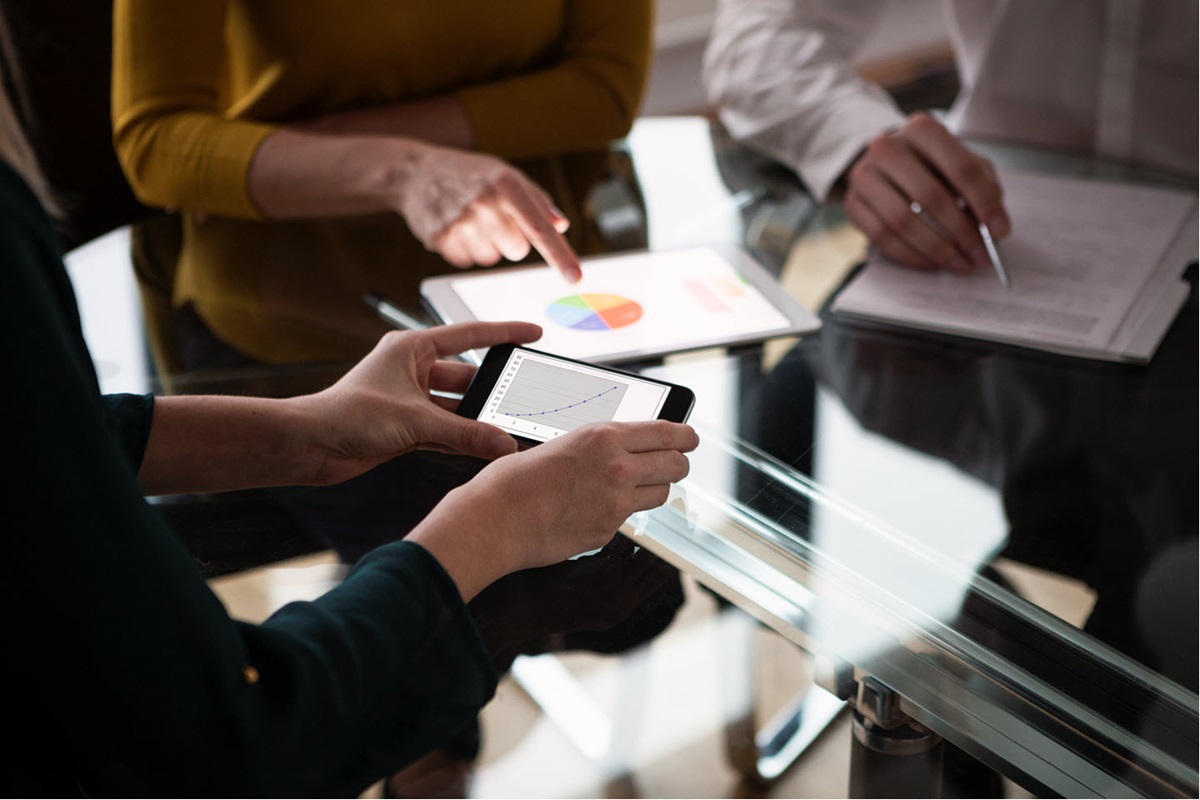 Close-up of a glass conference table as colleagues use smartphones, tablets, and paper documents to plan.