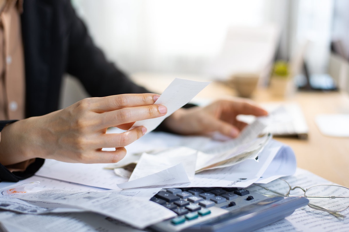 A home office worker sifts through a stack of receipts. A calculator rests under the stack of paper.