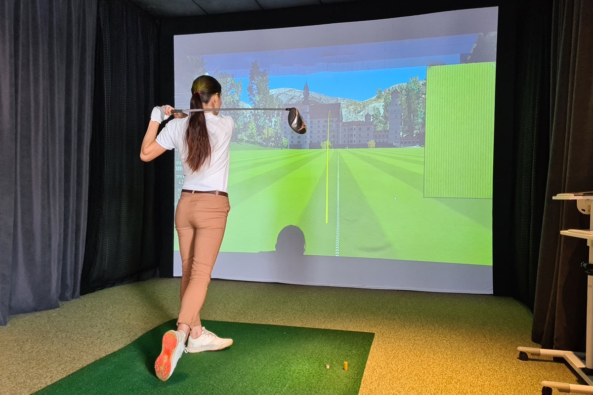 Young female swinging golf club in front of a projector. 