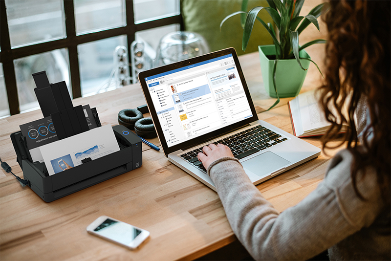 ScanSnap iX1300 scanner on a desk with a woman typing on a laptop