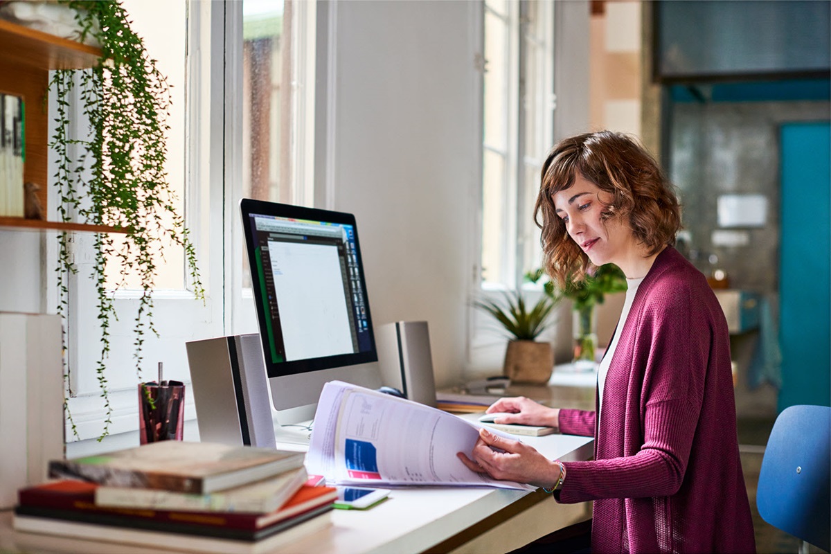 A woman reads over a typed document while sitting in front of a computer monitor.