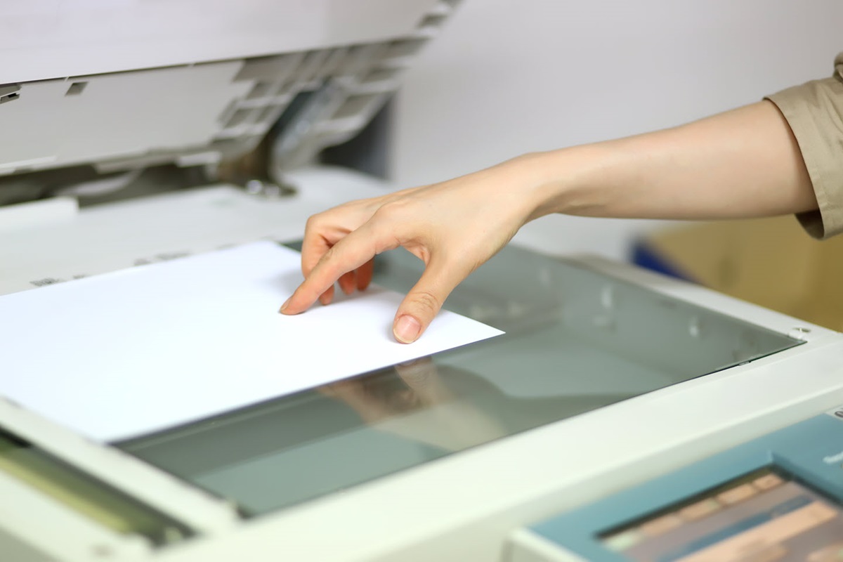 A person's hand holding a document against the glass pane of a scanner.