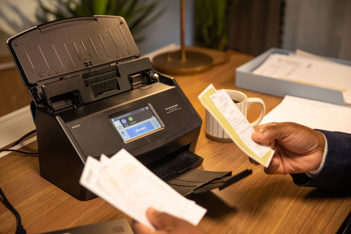 ScanSnap iX1600 Receipt Edition sitting on desk and hands of a man handling receipts in the foreground. 