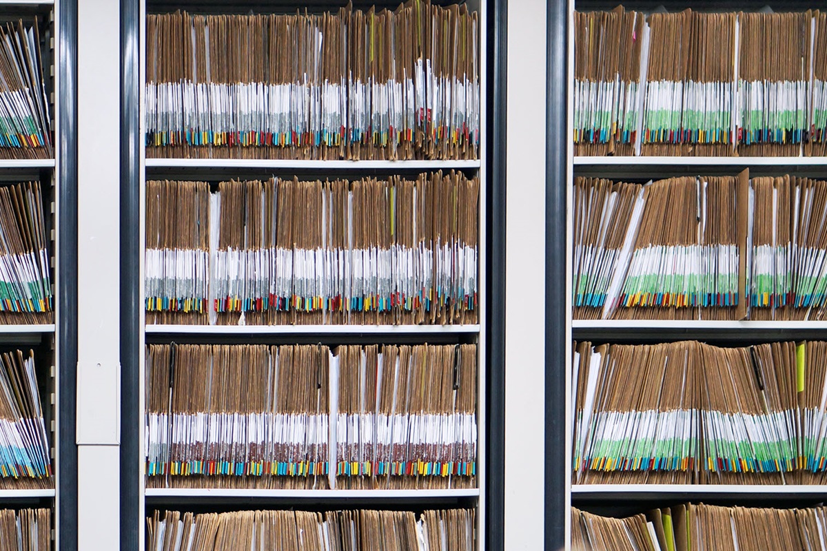 Three bookshelves filled with folders and folders of color-coded paper records.