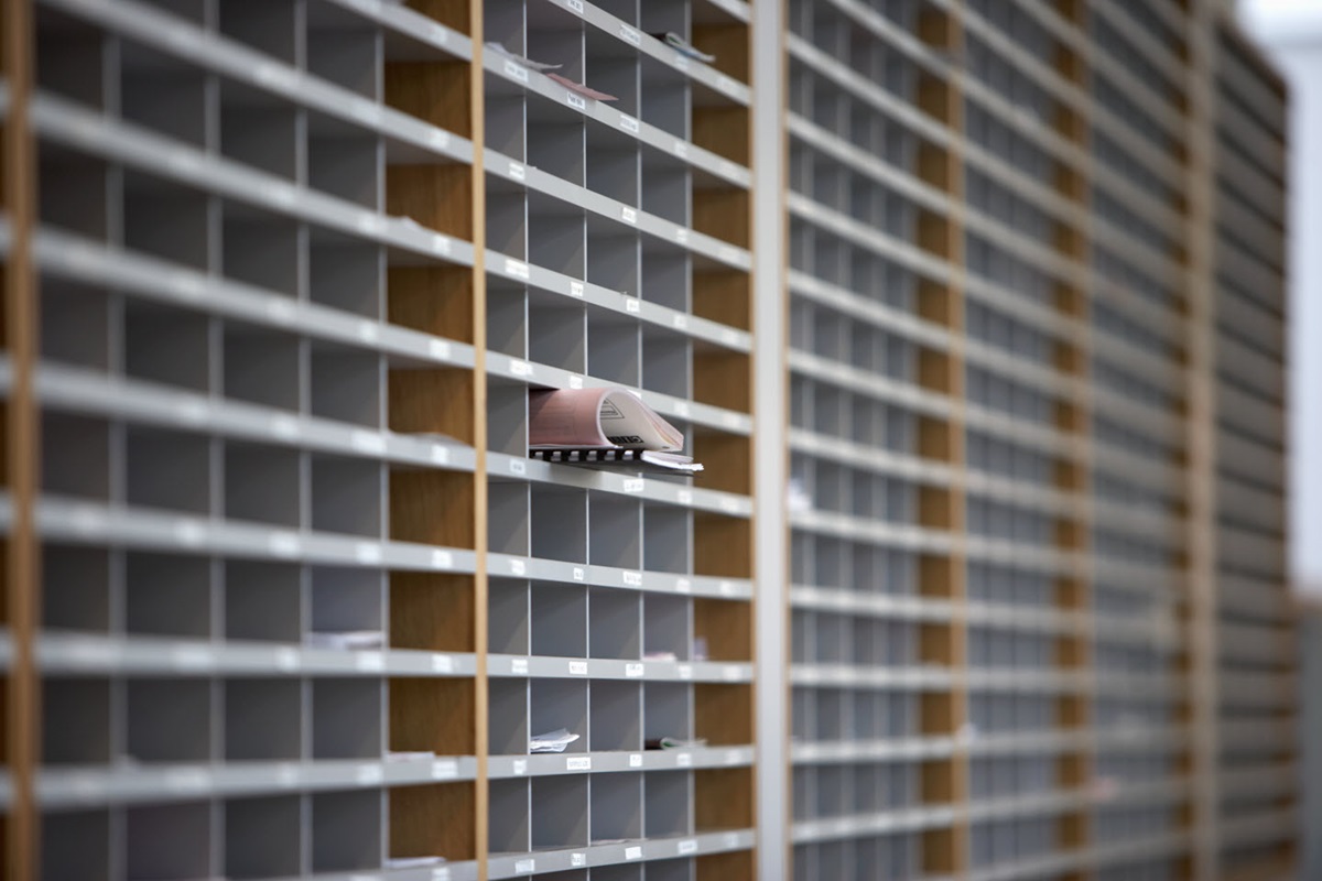A rolled up stack of papers sticks out of the middle tray of an office mailroom sorter.