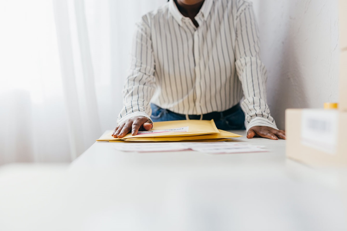A person wearing a striped shirt sorts mailer envelopes on a table.