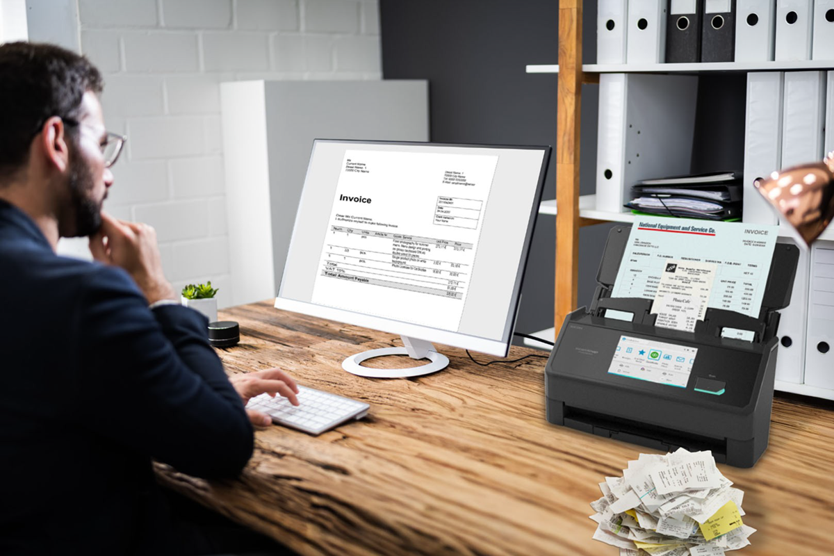 Man sitting at desk viewing invoice on computer with iX2500 scanner and receipts on desk. 
