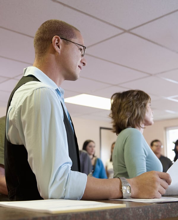 Man with glasses waiting in line with documents. 
