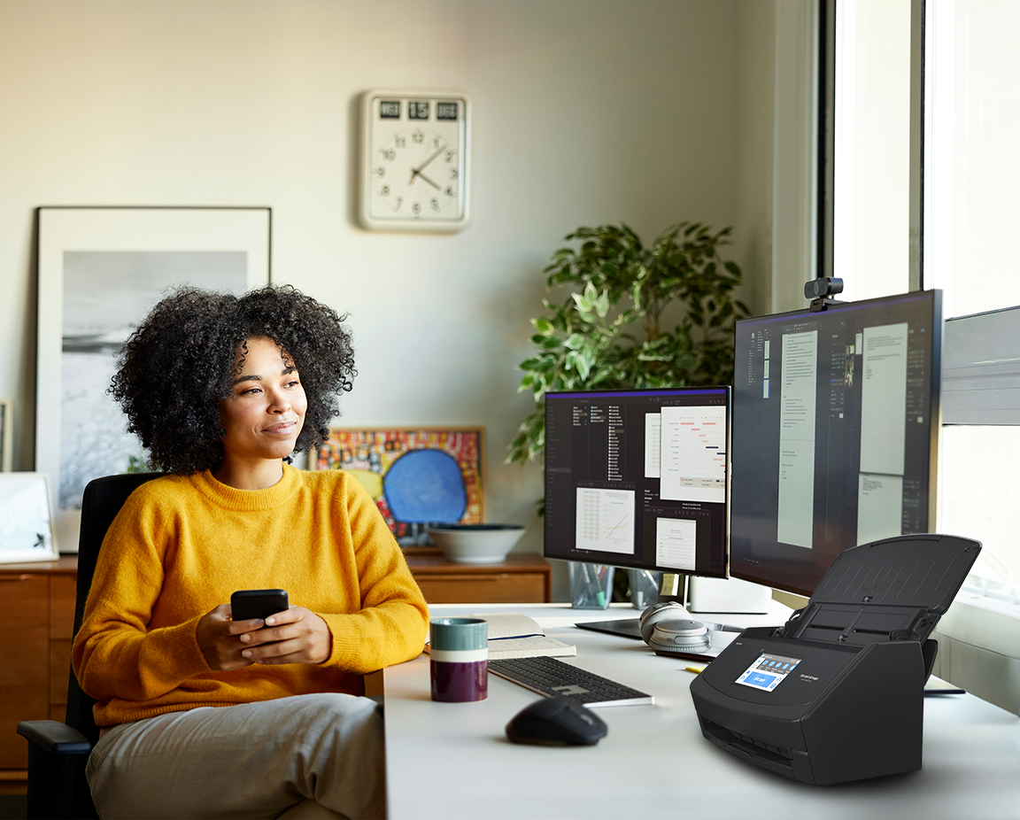 Woman typing on her phone at her desk with a ScanSnap iX1600