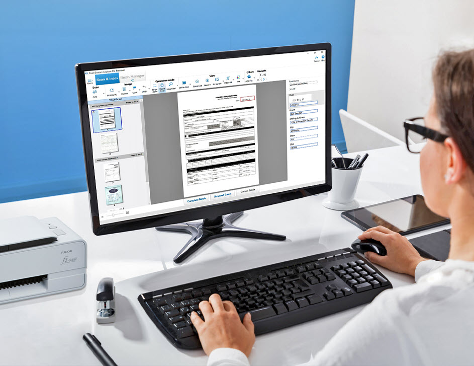 Woman at desk in front of keyboard and monitor with PaperStream Capture Pro Software UI on the screen.