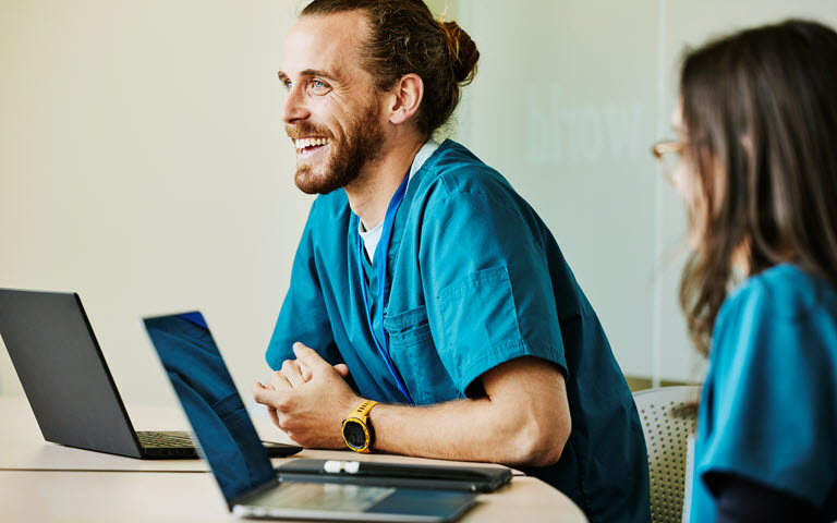 Two medical professionals in blue scrubs sitting with laptops.