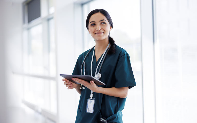 Female medical professional holding clipboard with a stethescope and badge around her neck.