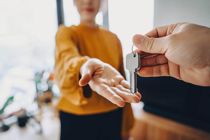 Woman with yellow shirt stretching hand out to receive set of keys.