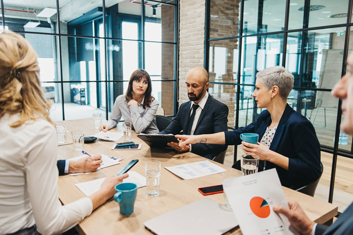 Group of financial executives working around a meeting table looking at tablet. 