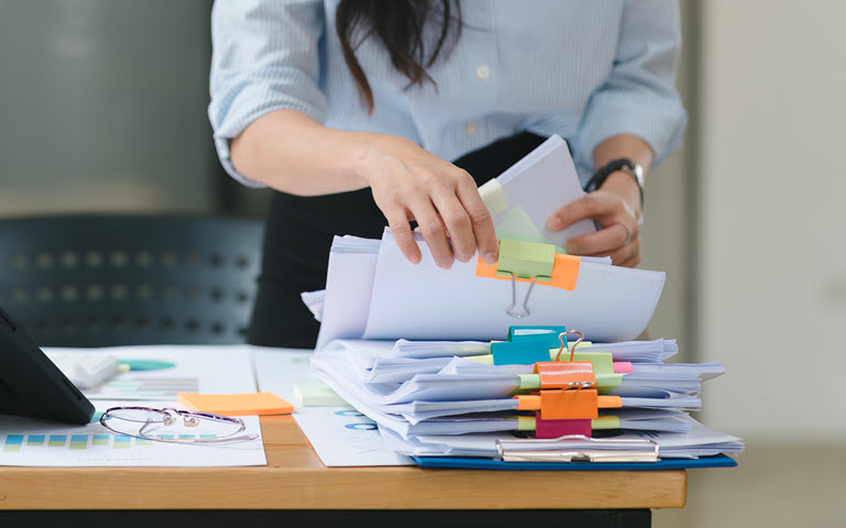 Woman handling stack of papers separated with bright Post It notes. 