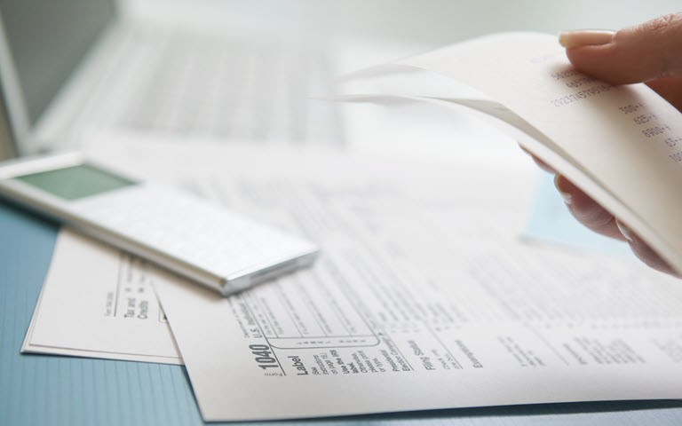 Woman with documents holding receipts with laptop.