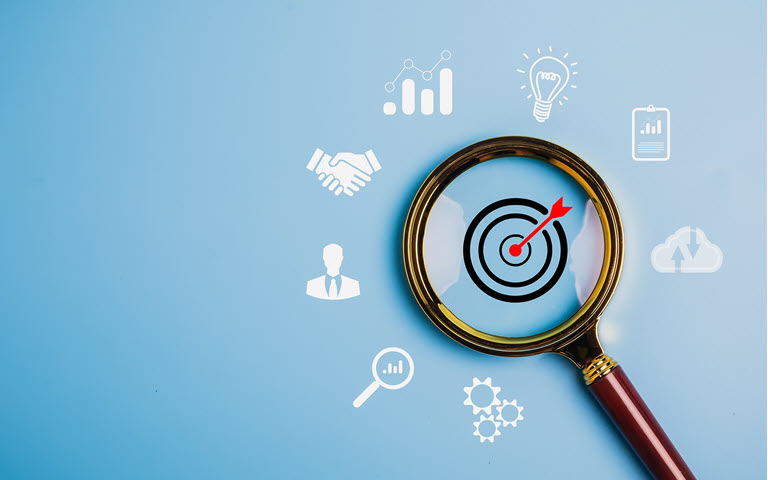 Magnifying glass with bulls eye in the middle of the lens surrounded by business icons.