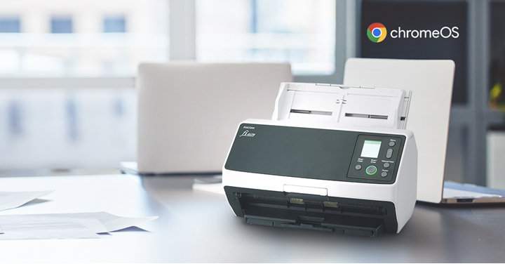 A RICOH Chromebook scanner and two laptops with papers nearby on a desktop.