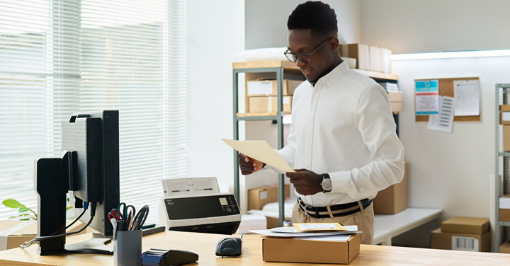 Man working at desk in an office setting using a Ricoh document scanner.