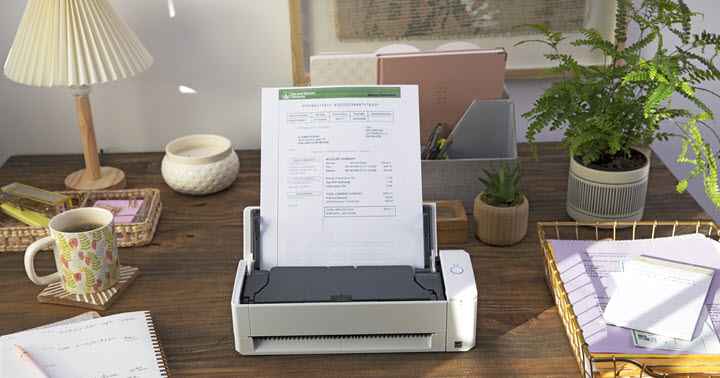ScanSnap iX1300 compact desktop scanner sitting on a desk with paper holder, plant, and coffee cup.