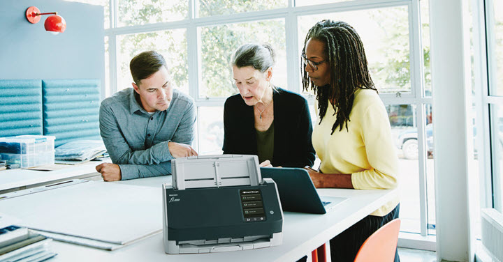 Three work colleagues collaborating in a bright office setting with a RICOH fi-8040 scanner.  