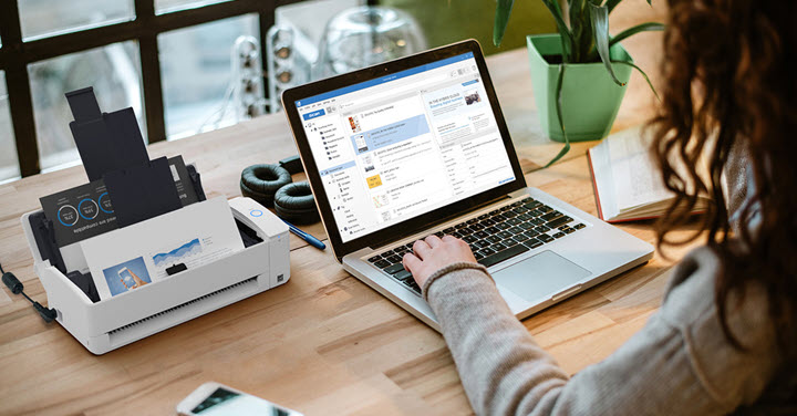 Image of woman working at a desk on a laptop scanning a document with a Ricoh ScanSnap iX1300 