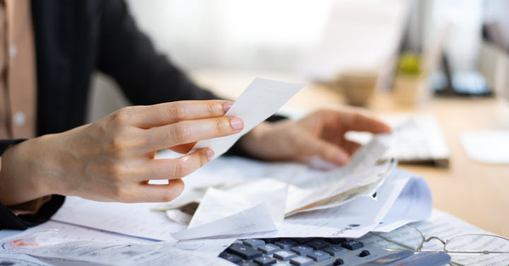 Woman looking through a pile of receipts with a calculator nearby. 