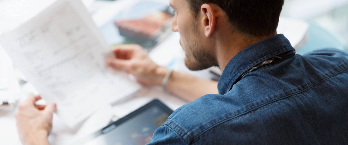 A businessman sits at a table looking over paper invoices.