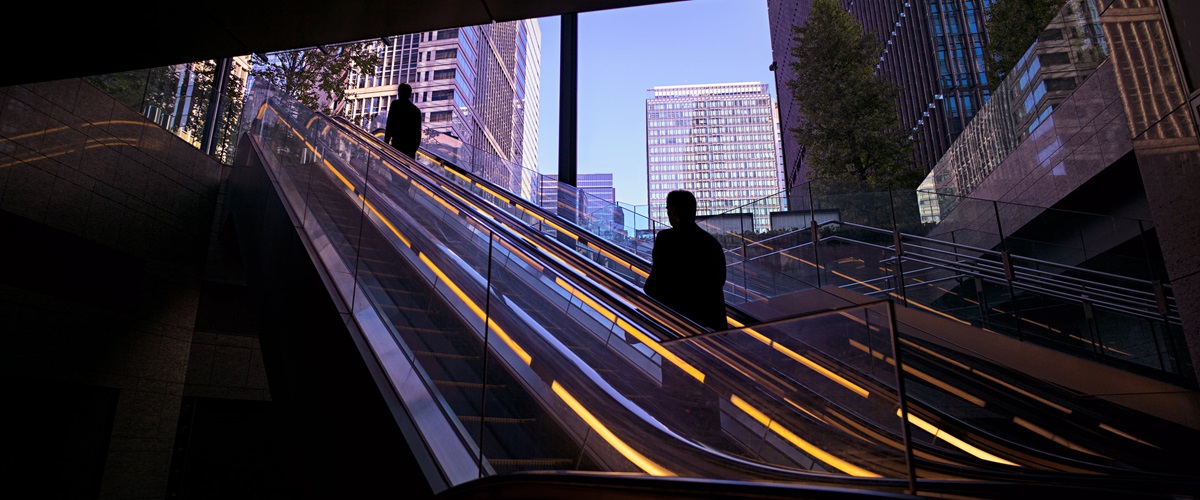 A businessperson exist the subway on an escalator heading toward a city business district.