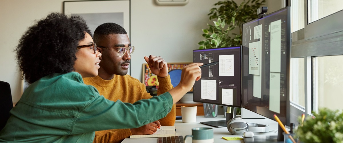 A man and a woman analyze data on two computer screens.