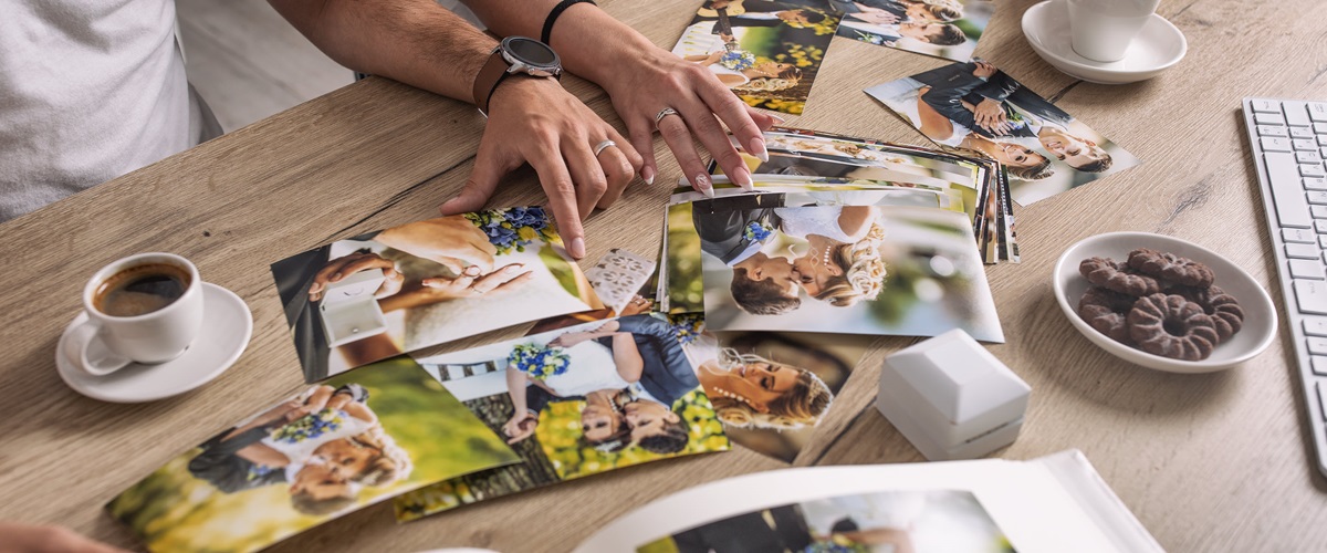 A married couple drinks coffee together while sorting through stacks of wedding photos.